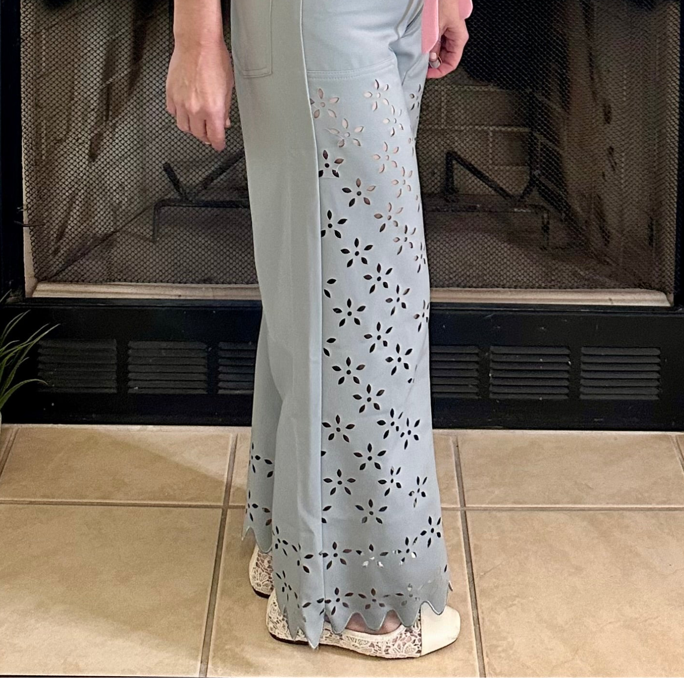 Person wearing a light-colored outfit with floral patterns in front of a fireplace.