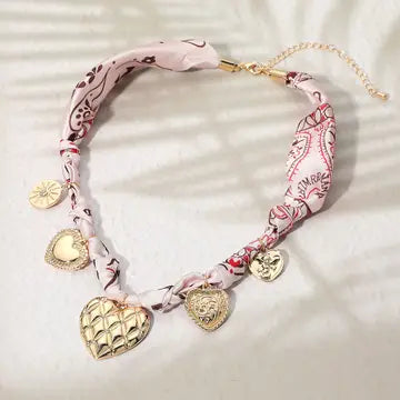 Necklace with heart-shaped charms and pink patterned strap on a light background