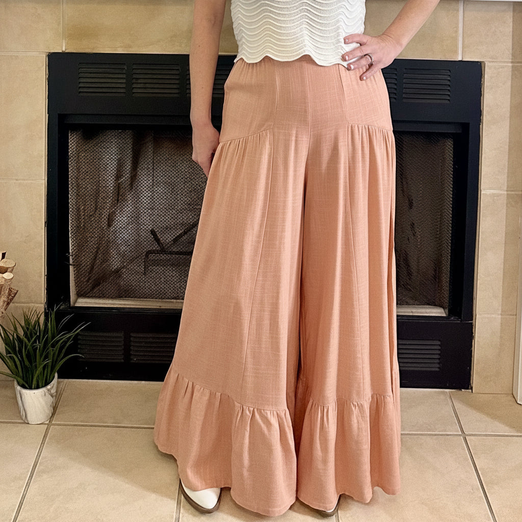 Person wearing peach-colored wide-leg pants standing in front of a fireplace.