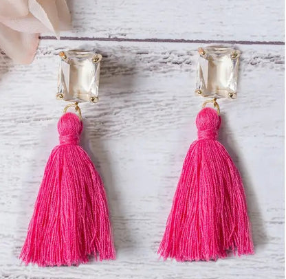 Pink tassel earrings with gold accents on a light wooden surface.