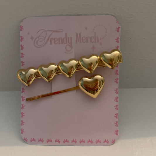 A gold heart-shaped hair accessory set displayed on a pink card labeled 'Trendy Merch,' photographed against a plain light background.