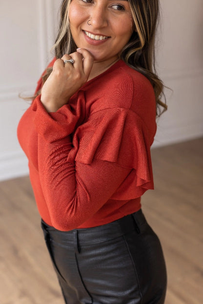 Rust  Ruffle Bodysuit, featuring a sleek, shimmering black fabric that perfectly balances boldness and grace. The cascading ruffle sleeves and flared cuffs create a dramatic silhouette. 