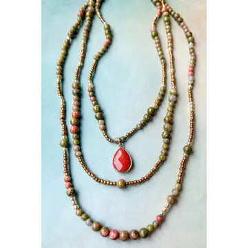Two beaded necklaces with a red teardrop pendant on a light blue background