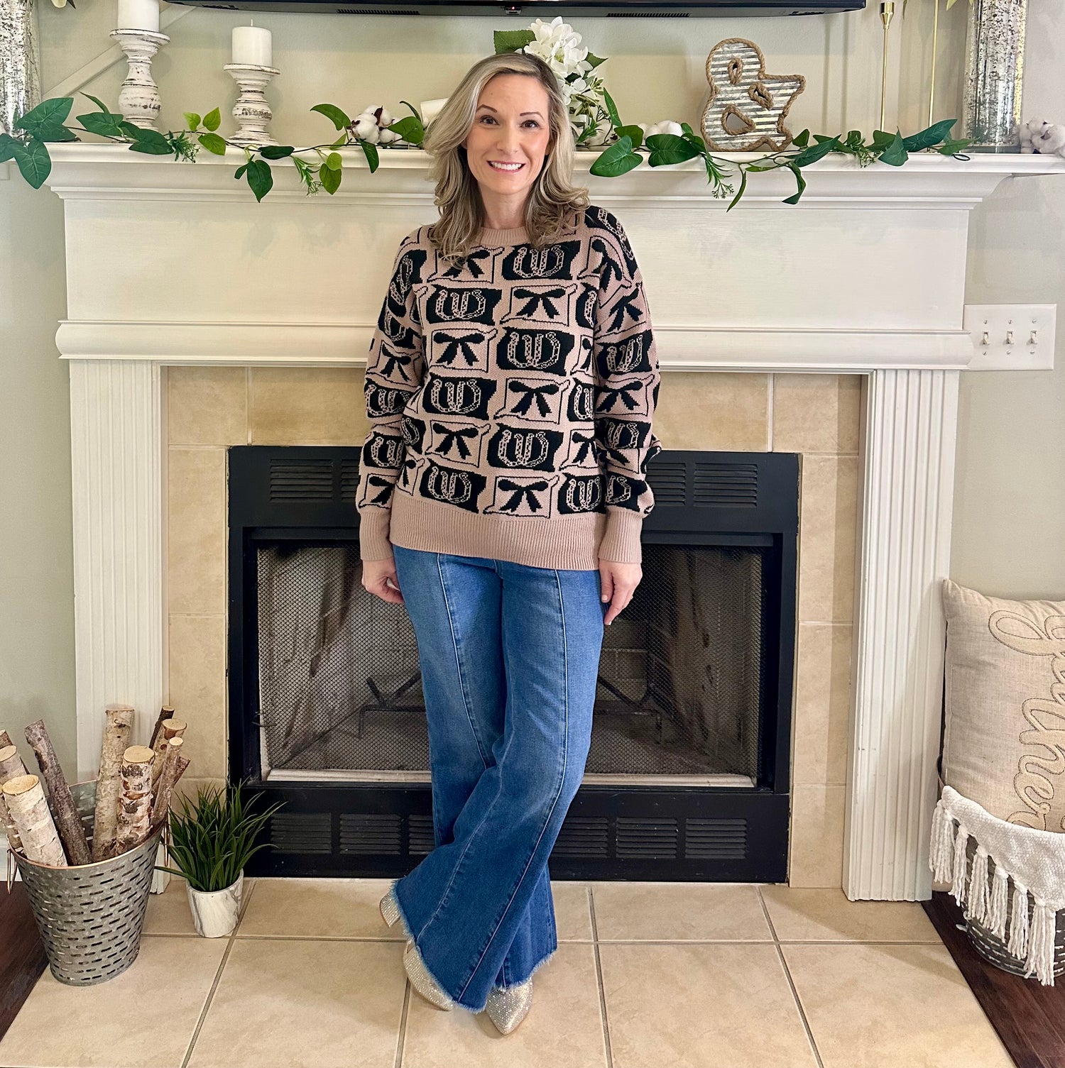 Woman standing in front of a fireplace wearing a patterned sweater and blue jeans.