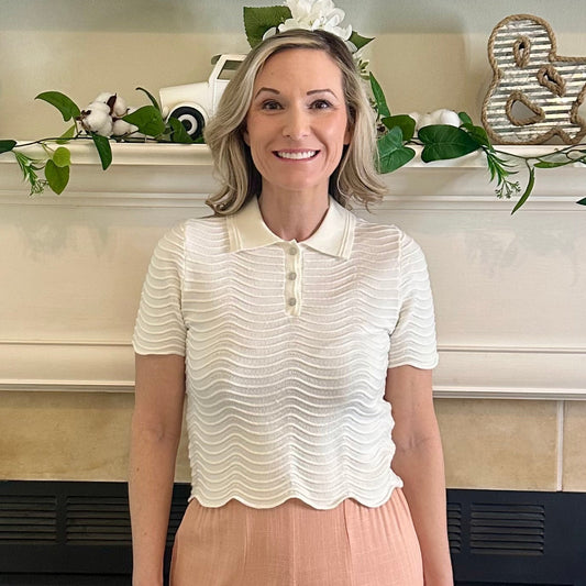 Woman standing in front of a decorated fireplace wearing a white blouse and peach pants.