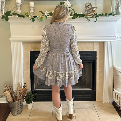Person wearing a gray floral dress standing in front of a fireplace.