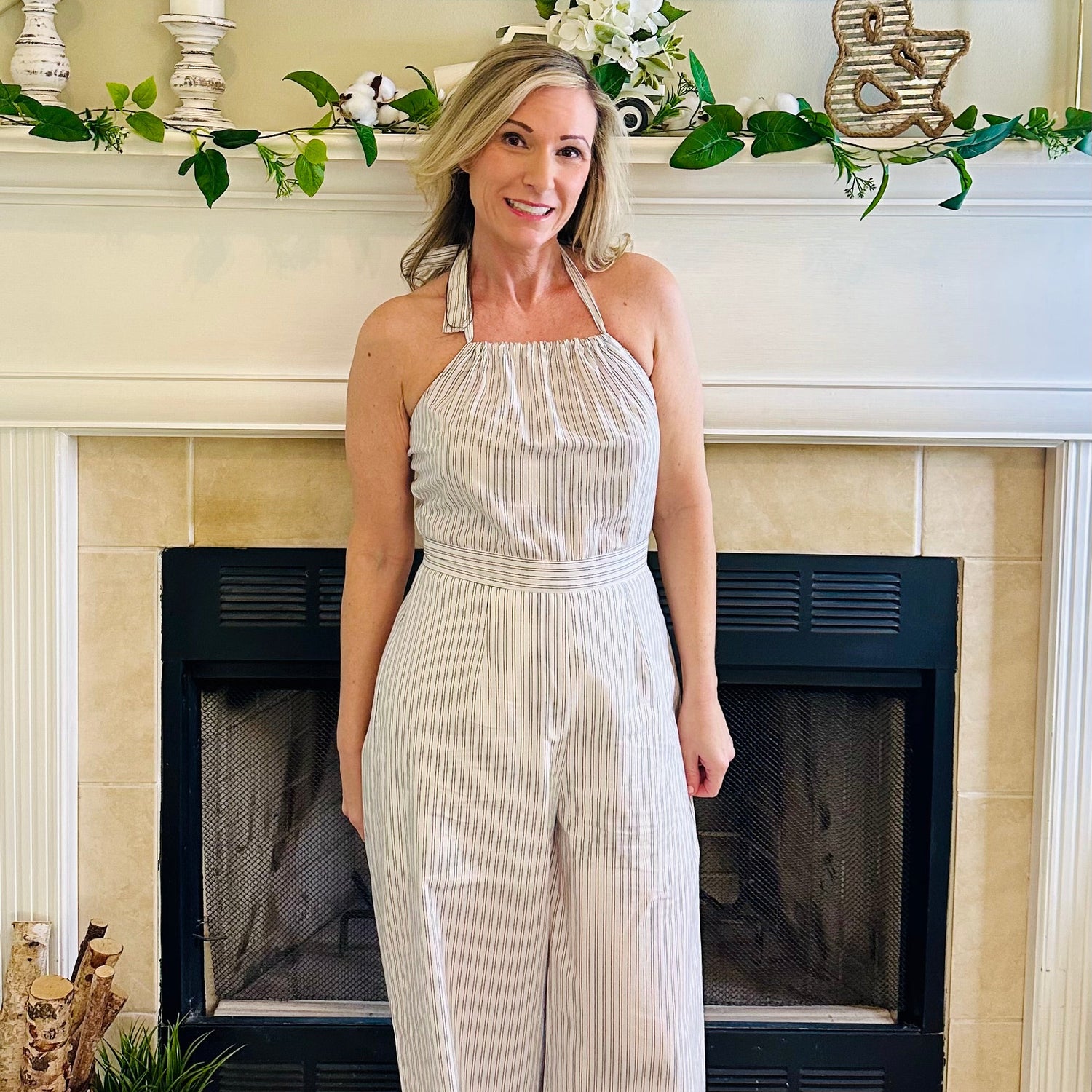 Woman in a white striped jumpsuit standing in front of a fireplace with decorative elements.