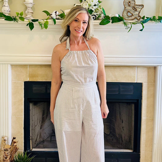 Woman in a white striped jumpsuit standing in front of a fireplace with decorative elements.