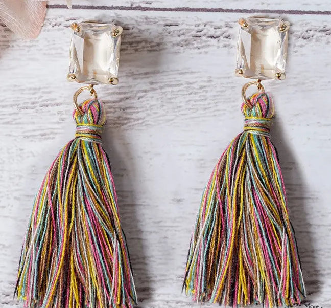 Multicolored tassel earrings with square gemstones on a light wooden surface.