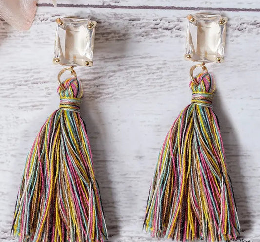 Multicolored tassel earrings with square gemstones on a light wooden surface.