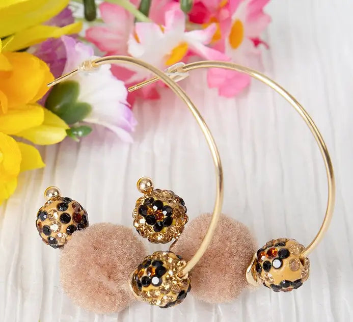 Gold hoop earrings with pom-pom and bead details on a floral background