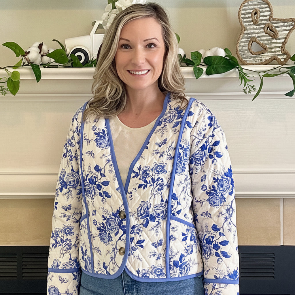 Woman wearing a floral jacket and jeans standing in front of a fireplace.