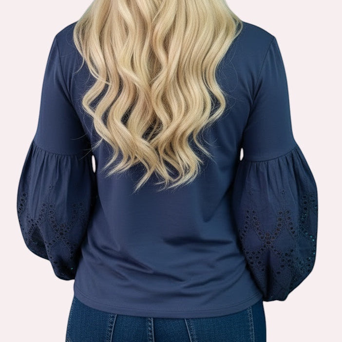 Woman wearing a navy blue top with lace sleeves against a teal and white geometric wall.