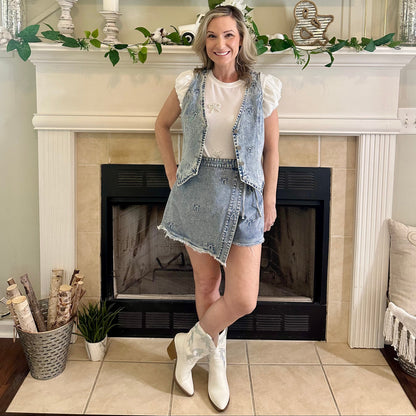 Woman in denim outfit standing in front of a fireplace with decorative items.