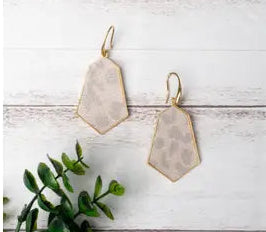 Beige earrings on a white wooden surface with a green plant