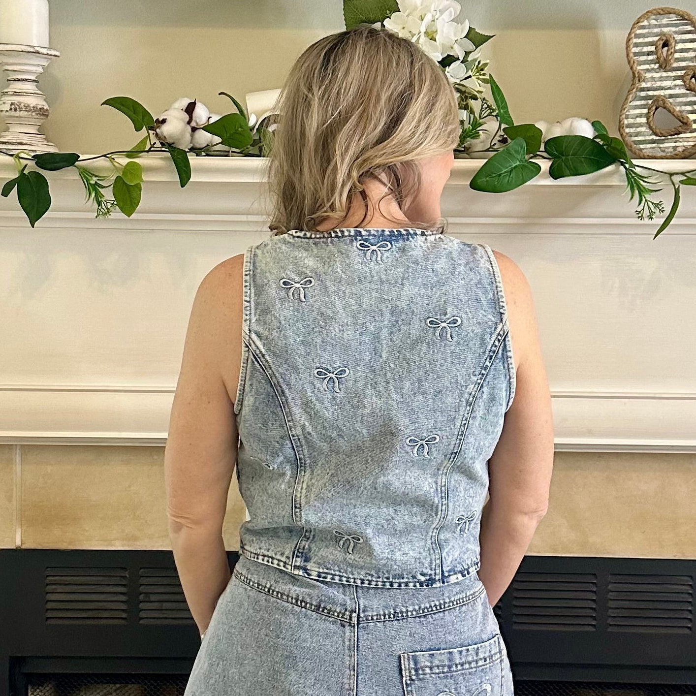 Person wearing a denim dress with decorative bows in front of a decorated fireplace.