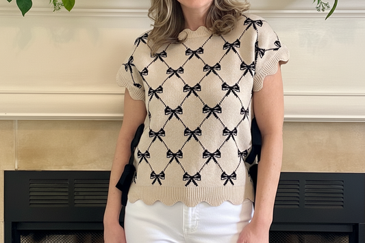 Person wearing a beige sweater with black bow pattern in front of a fireplace.