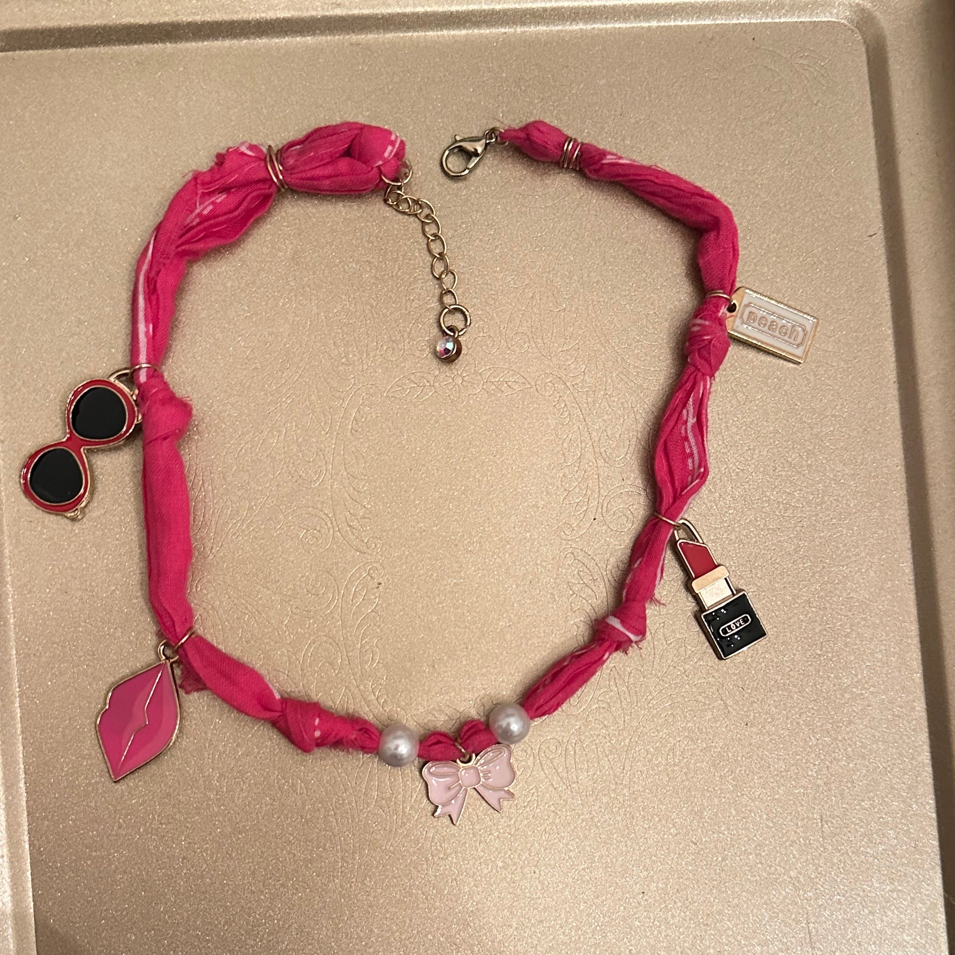 Pink ribbon necklace with leaf and heart charms on a beige tray