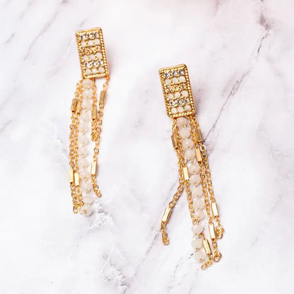 Gold and pearl earrings on a white textured background