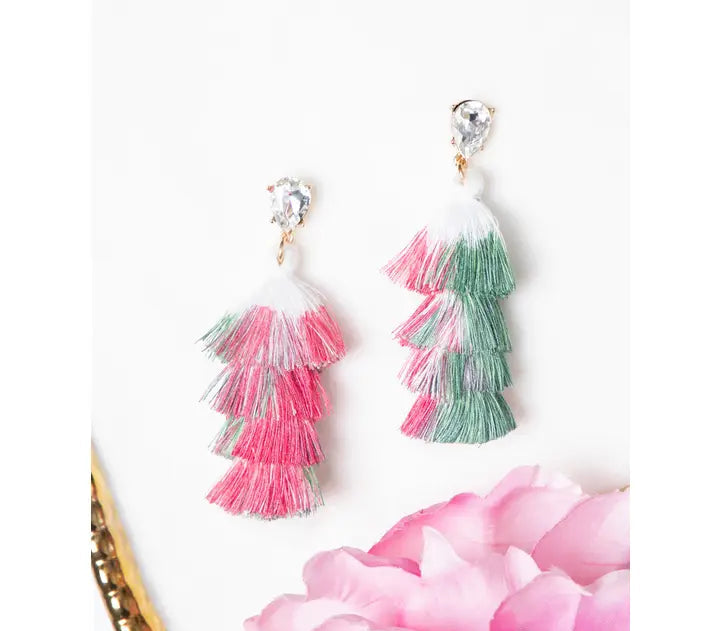 Tassel earrings with pink and green tassels on a white background with a pink flower and gold object.