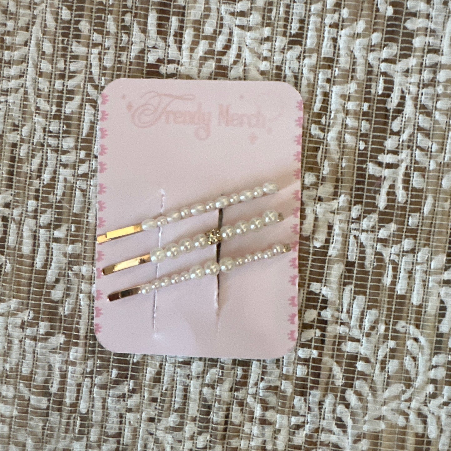 Three gold hair pins decorated with white pearls, displayed on a pink card labeled 'Fancy Nerd' and resting on a textured beige lace fabric background.