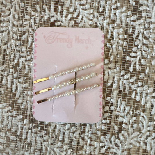 Three gold hair pins decorated with white pearls, displayed on a pink card labeled 'Fancy Nerd' and resting on a textured beige lace fabric background.