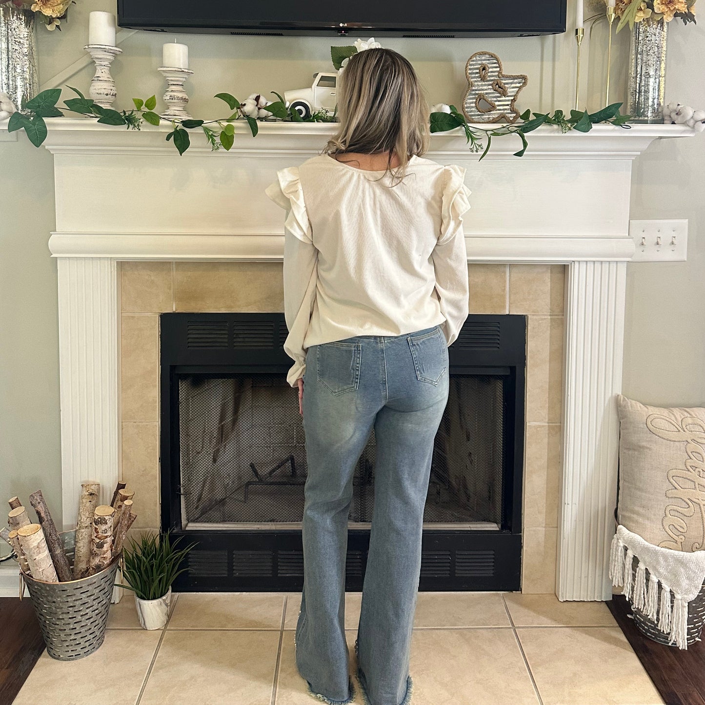 Person standing in a living room with a television, fireplace, and decorative items.