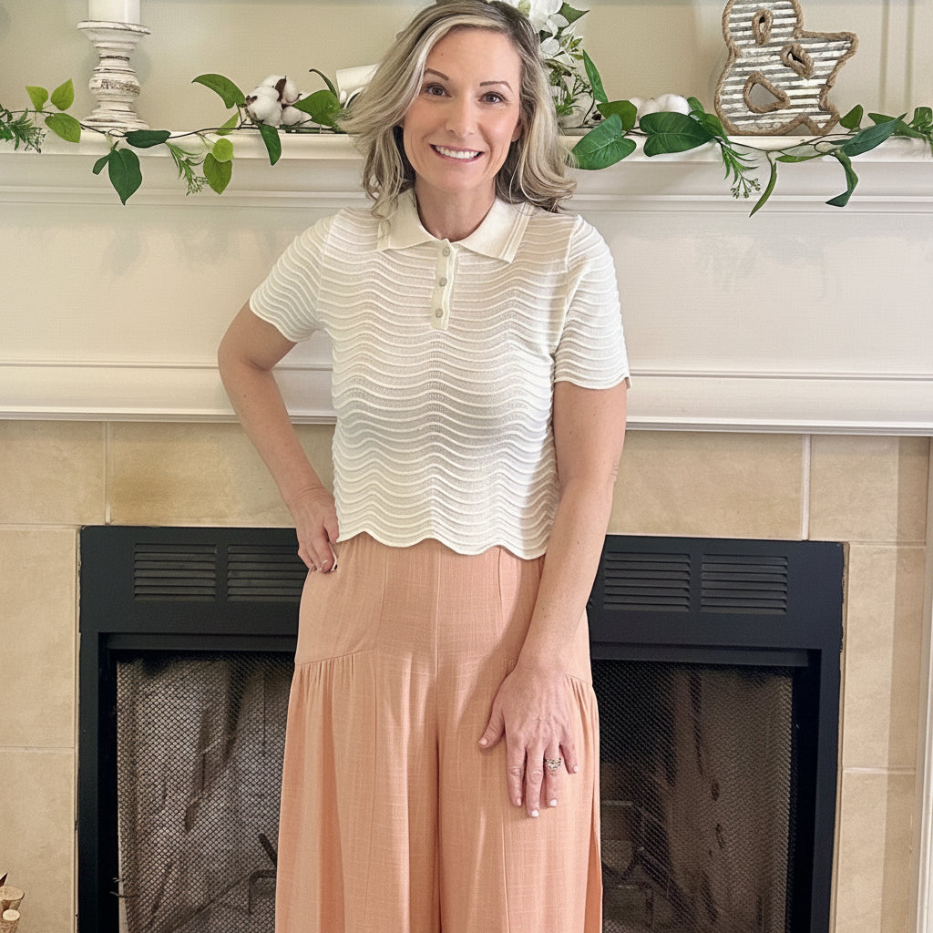 Woman in a white top and peach skirt standing in front of a fireplace.