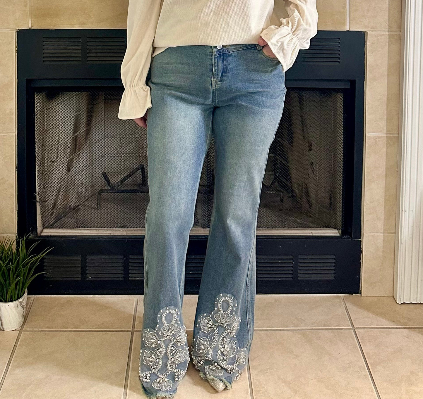 Person wearing blue jeans with decorative cuffs in front of a fireplace.