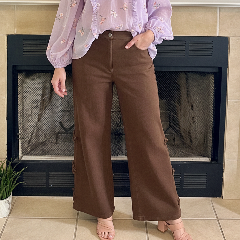 Woman standing in front of a fireplace wearing a cream sweater and brown pants.