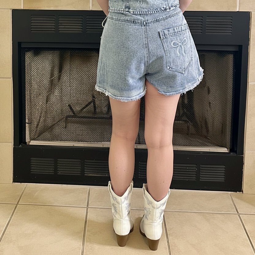 Person wearing a denim romper standing in front of a fireplace.