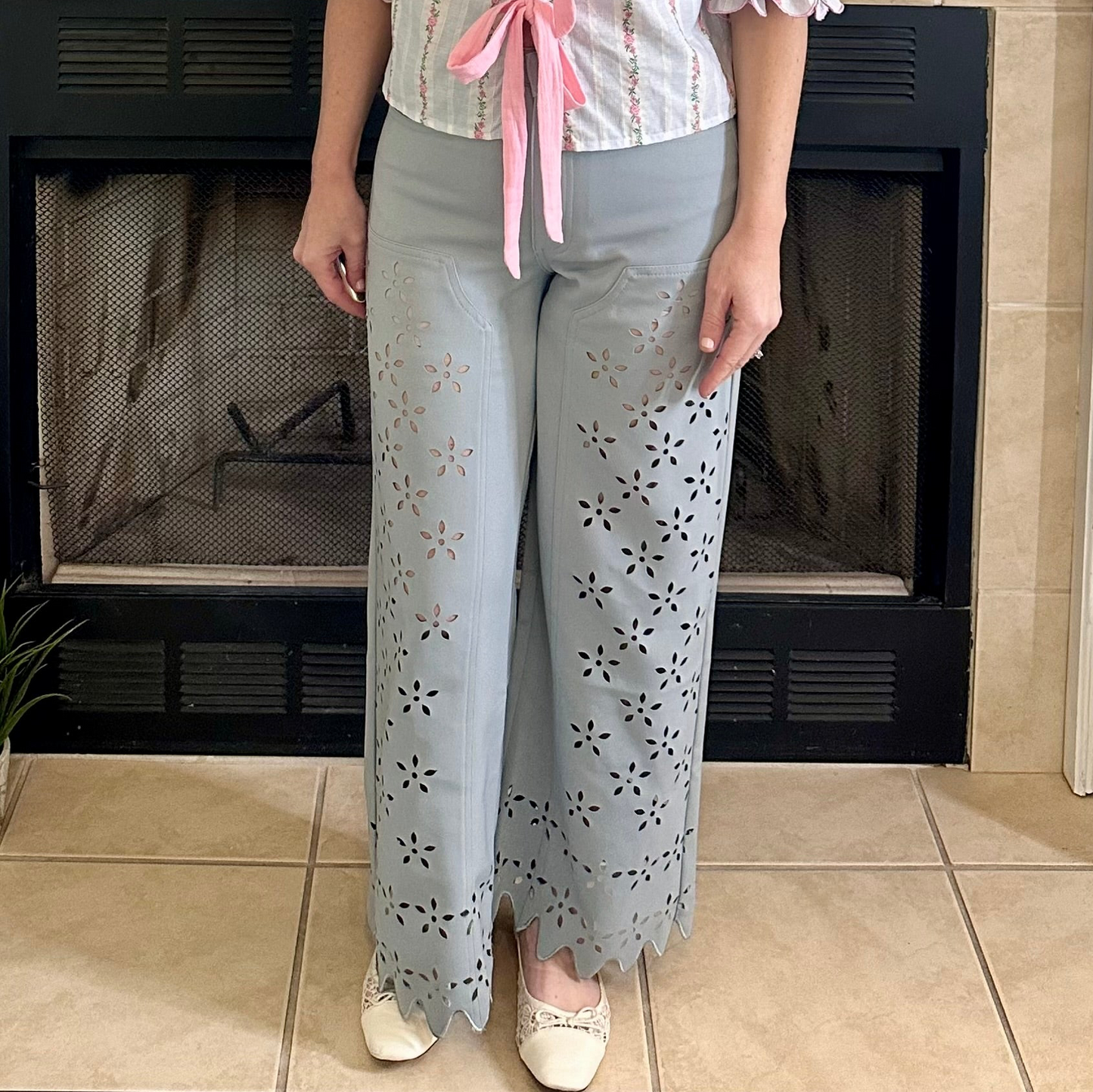 Person wearing light blue pants with floral cut-out design in front of a fireplace.