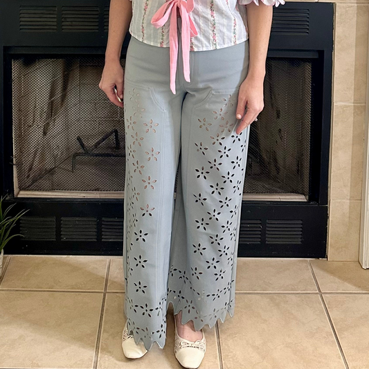 Person wearing light blue pants with floral cut-out design in front of a fireplace.