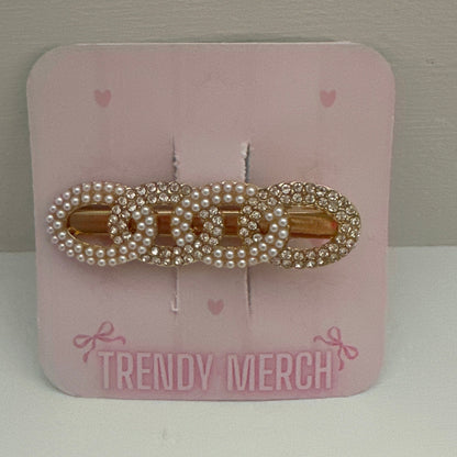 A gold-tone hair claw clip embellished with white faux pearls, displayed on a pink card labeled 'TRENDY MERCH' against a neutral gray background.