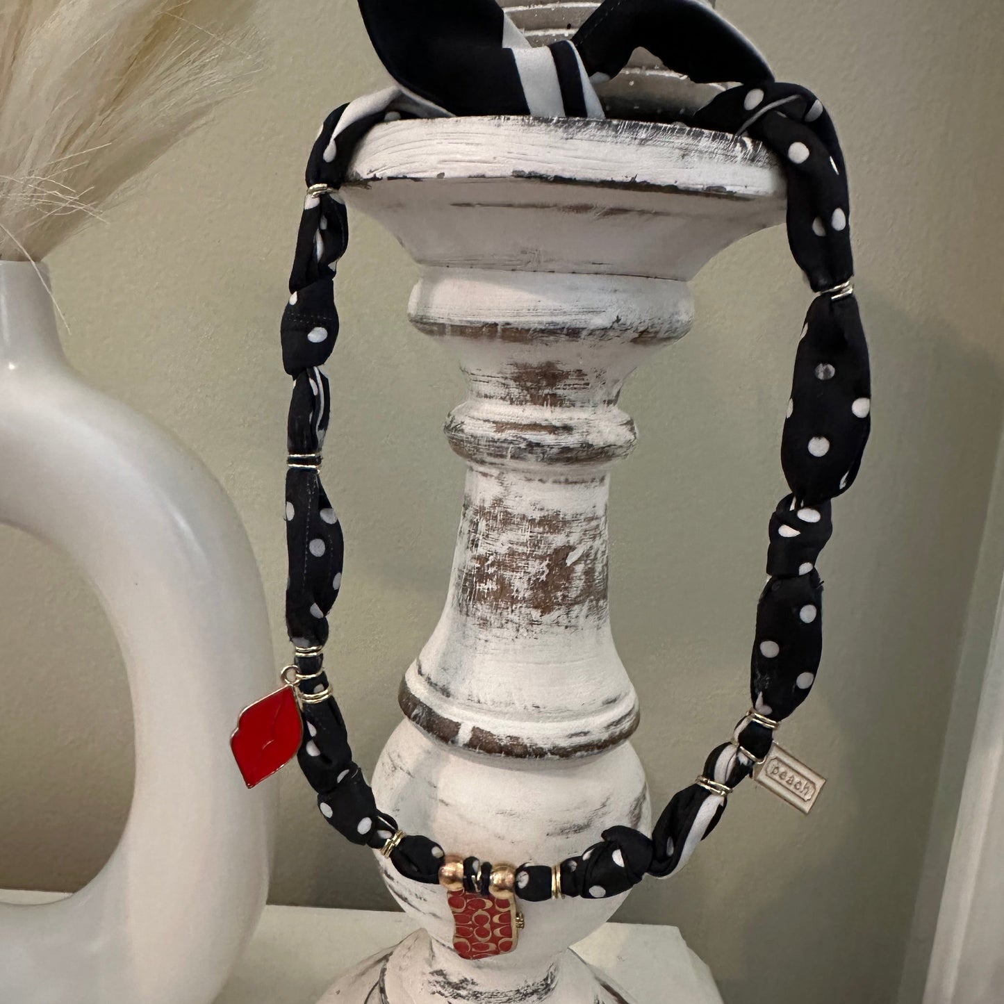 A black and white polka dot fabric belt with silver-tone hardware and a small red tag, draped over a distressed white wooden candle holder.