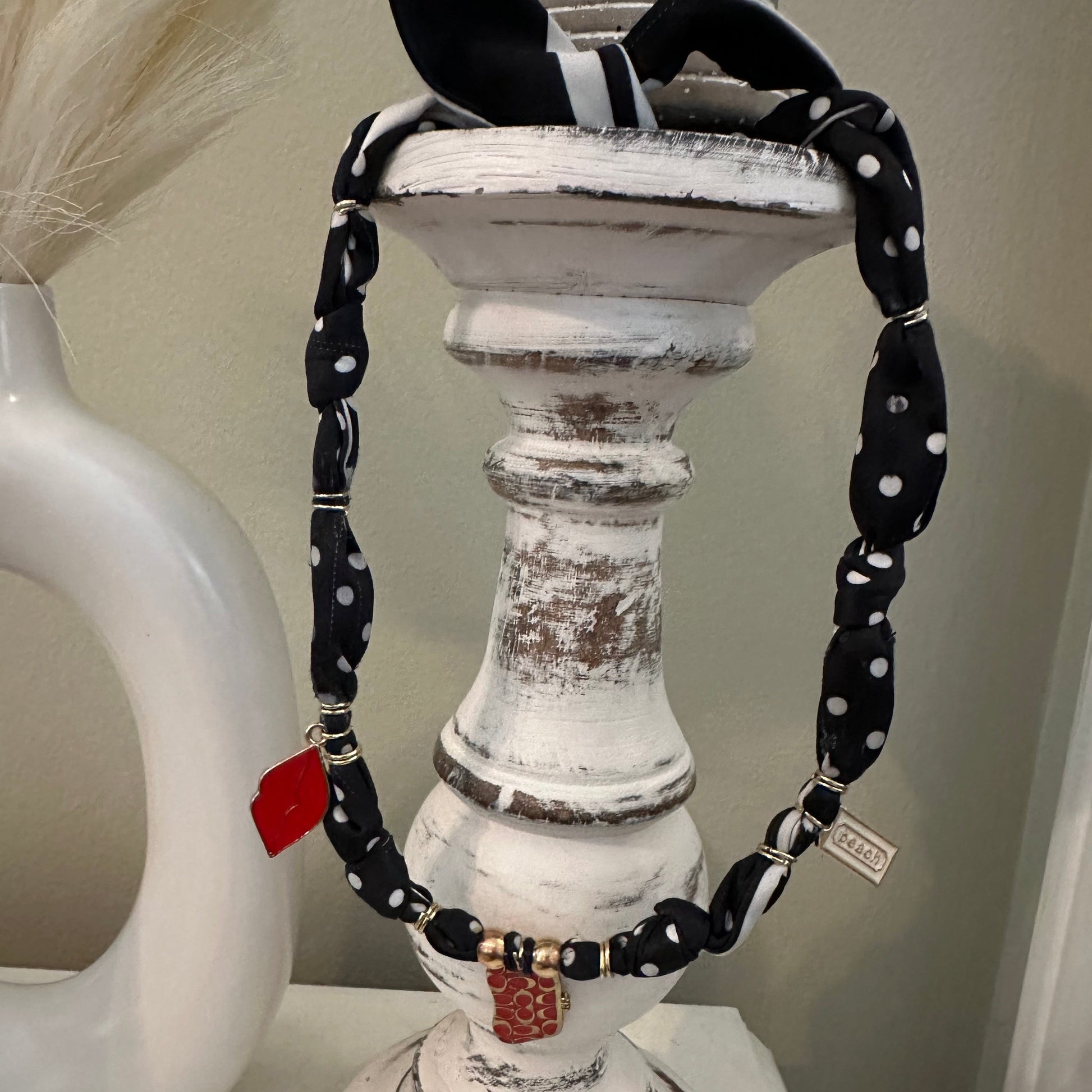 A black and white polka dot fabric belt with silver-tone hardware and a small red tag, draped over a distressed white wooden candle holder.