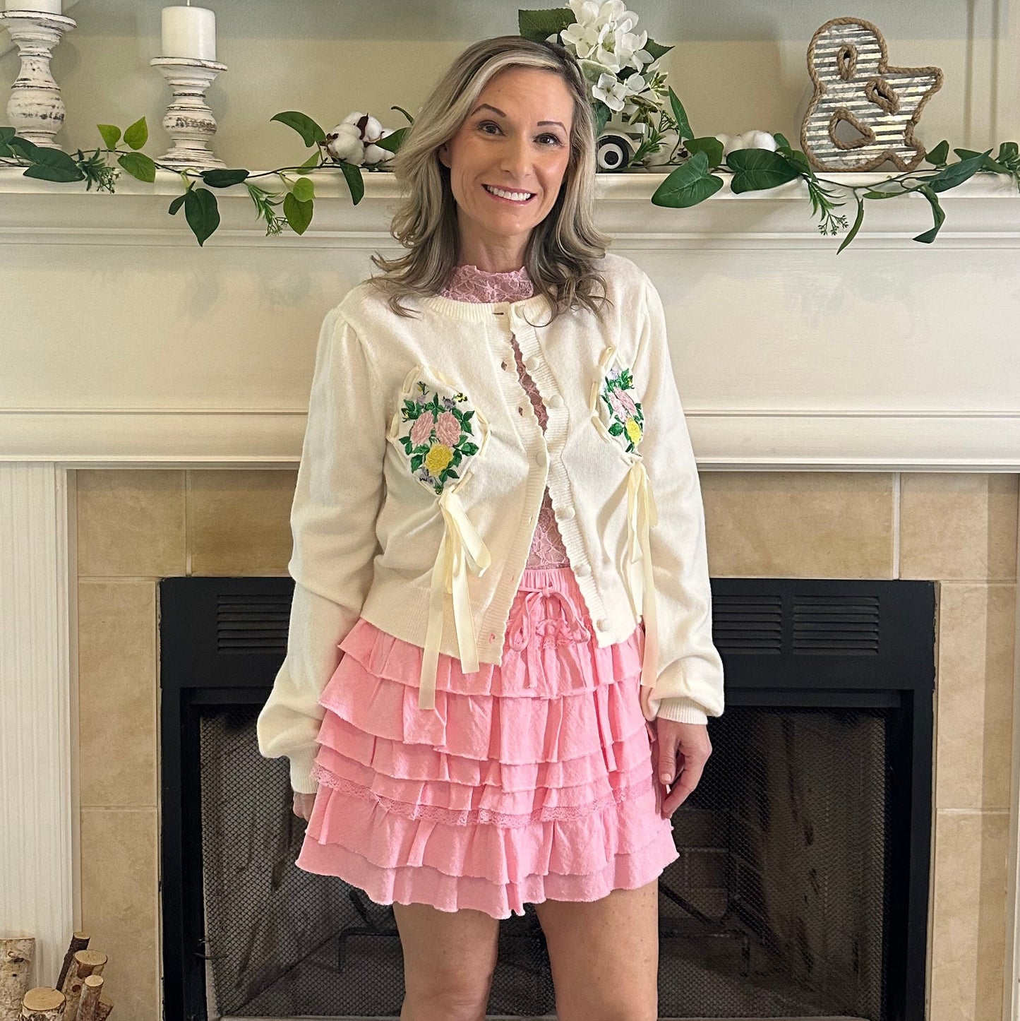 Person wearing a white blouse with floral details and a pink skirt in a room with decorative elements.