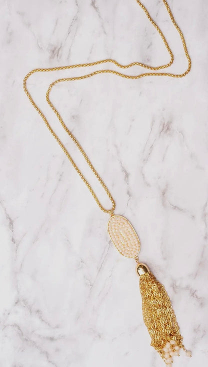 Gold necklace with a tassel pendant on a marble surface