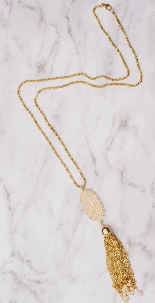 Gold necklace with a tassel pendant on a marble surface