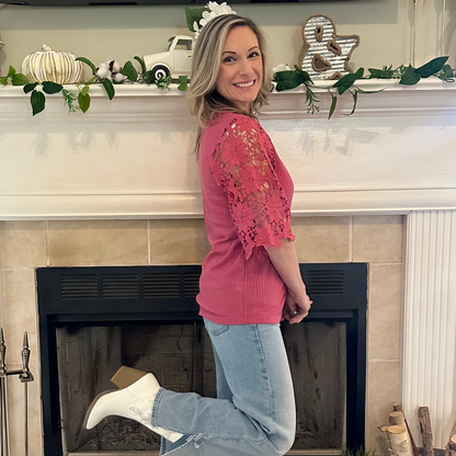 Woman in pink top and jeans standing in front of a fireplace with decorative items on the mantel.