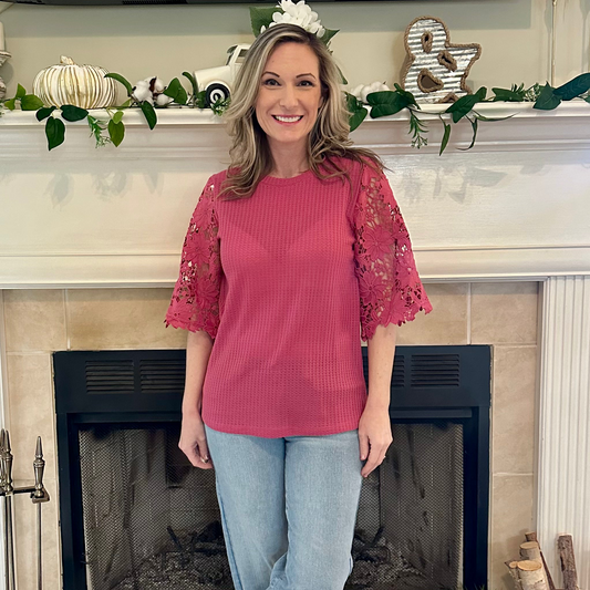 Woman wearing a pink top with lace sleeves in front of a decorated fireplace.
