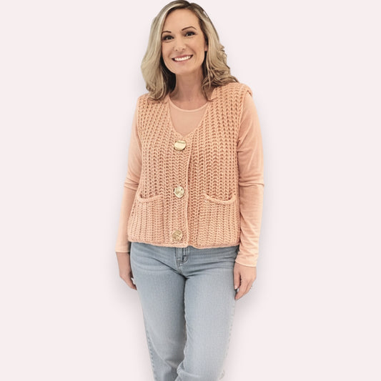 Woman wearing a beige knitted vest over a pink shirt with light blue jeans on a beige background