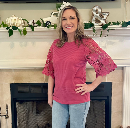 Woman wearing a pink blouse with lace sleeves in front of a decorated fireplace.