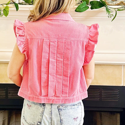 A woman viewed from behind wearing a pink and white vertically striped ruffle-sleeve crop top, standing in front of a fireplace.