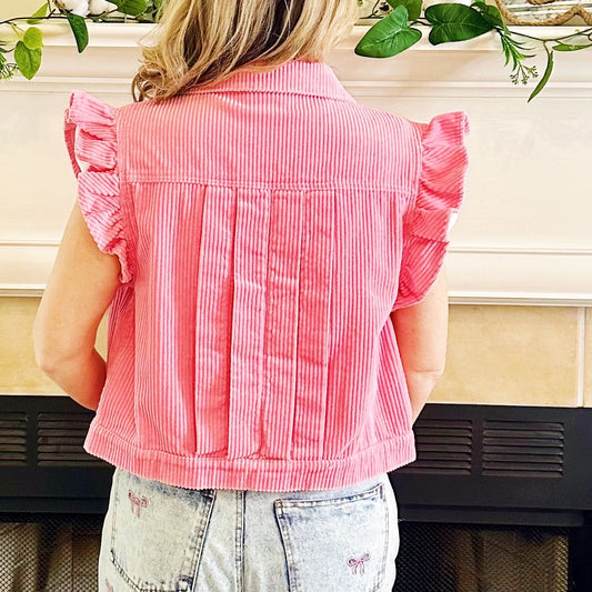 A woman viewed from behind wearing a pink and white vertically striped ruffle-sleeve crop top, standing in front of a fireplace.