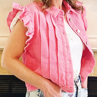 A woman wearing a pink corduroy sleeveless vest with ruffled shoulders over a white top and light blue jeans.
