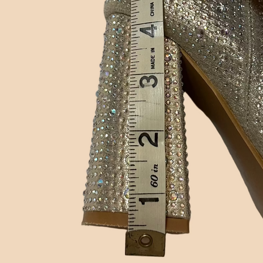 Silver glittery high-heeled shoe with a measuring tape showing the heel height on a beige background