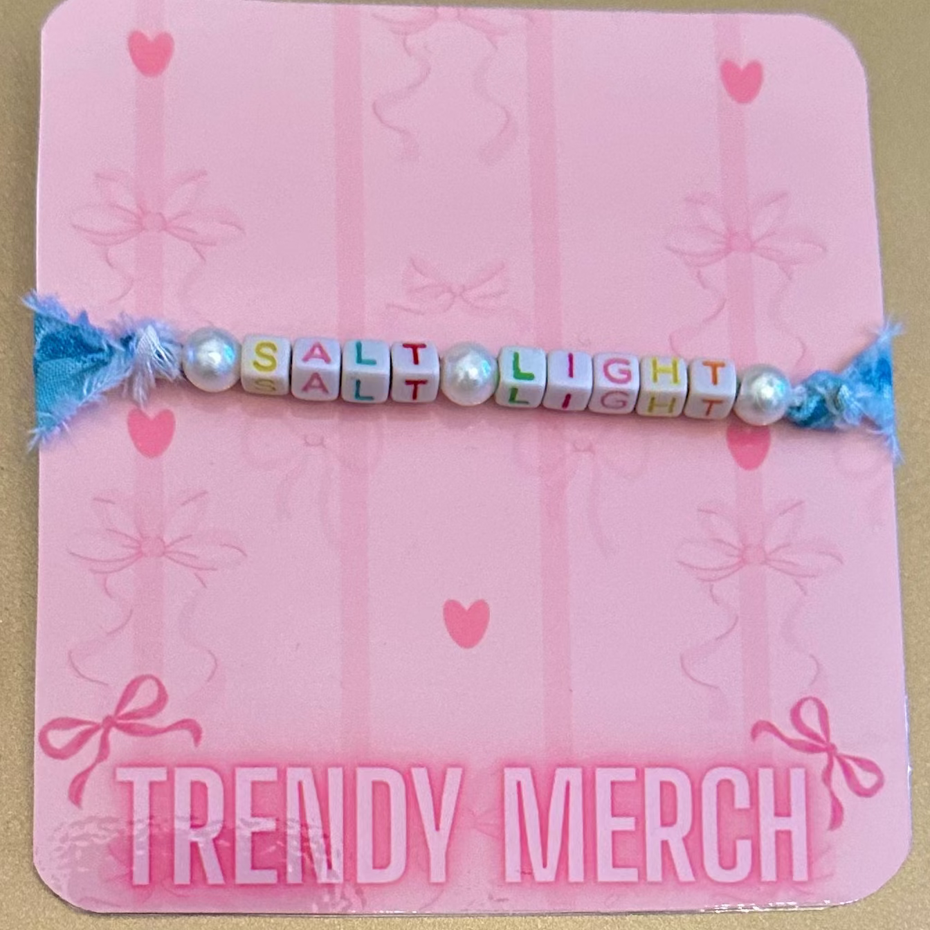 Pink card with 'TRENDY MERCH' text and a colorful bracelet on a beige background