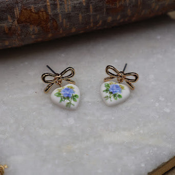 Pair of earrings with floral design and gold bows on a textured surface