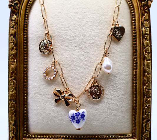 Charm Necklace. This gold-tone necklace features a combination of unique, eye-catching charms, including a delicate pearl, a floral-inspired heart, and intricate coin pendants.